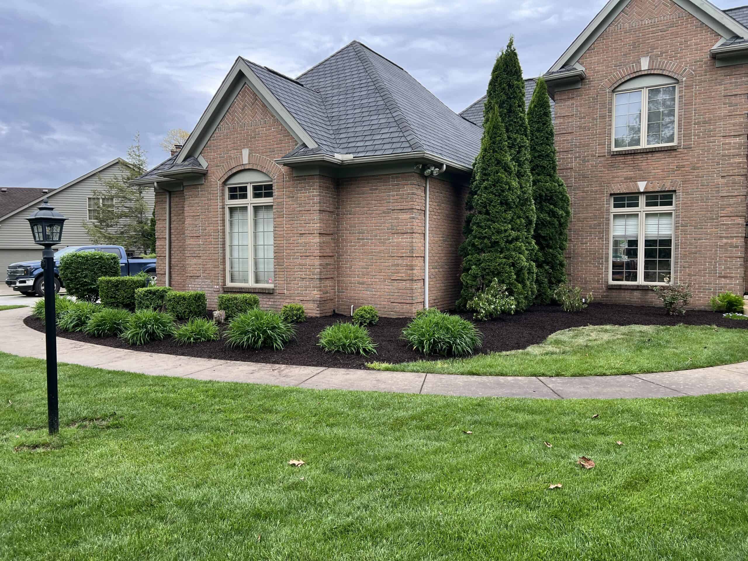 A well-maintained brick home with a lush green lawn, fresh mulch, and neatly trimmed shrubs under a cloudy sky.