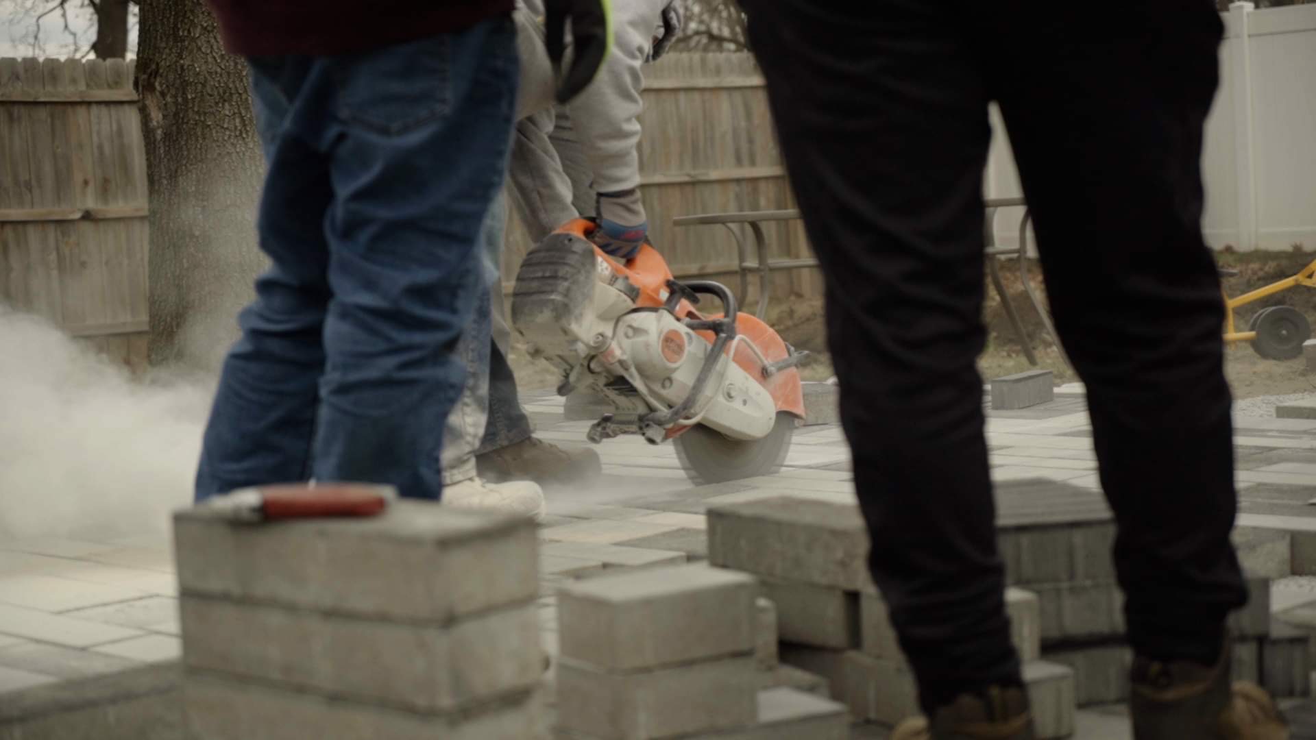 A team of people laying down patio pavers and cutting them down