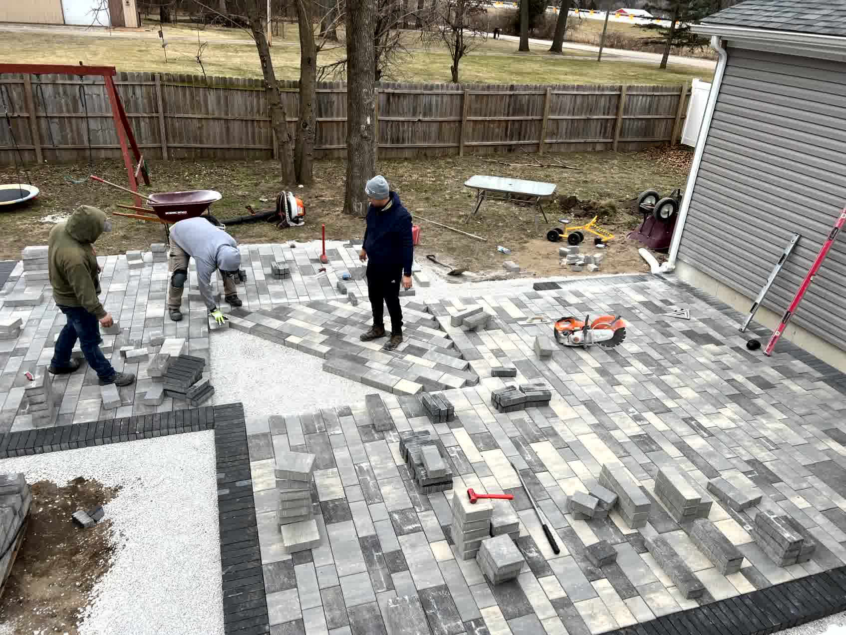 Crew installing gray brick pavers in backyard patio, creating a durable and stylish outdoor living space.