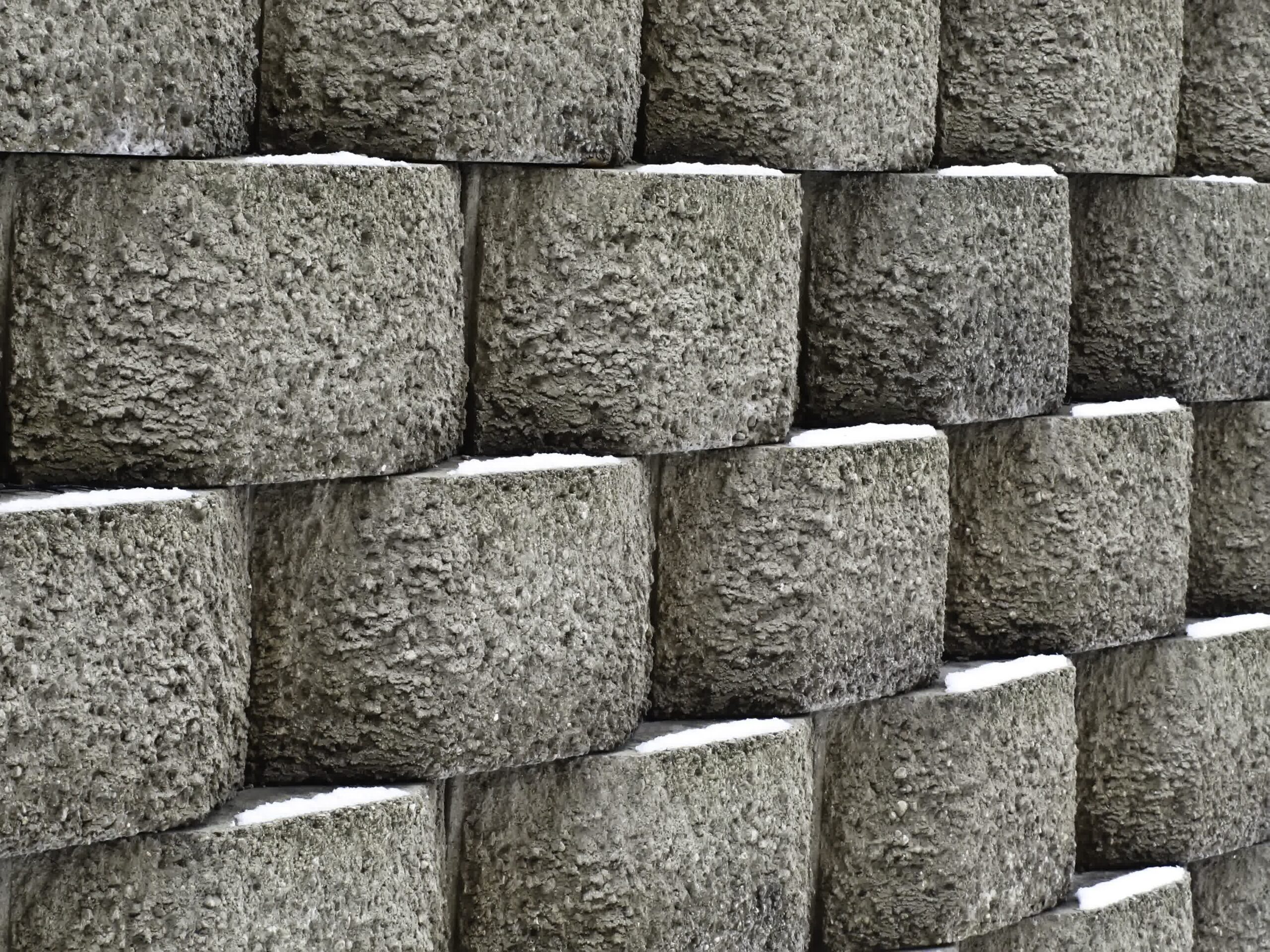Close-up of stacked concrete retaining wall blocks with textured surfaces and snow buildup between rows, showcasing durability.