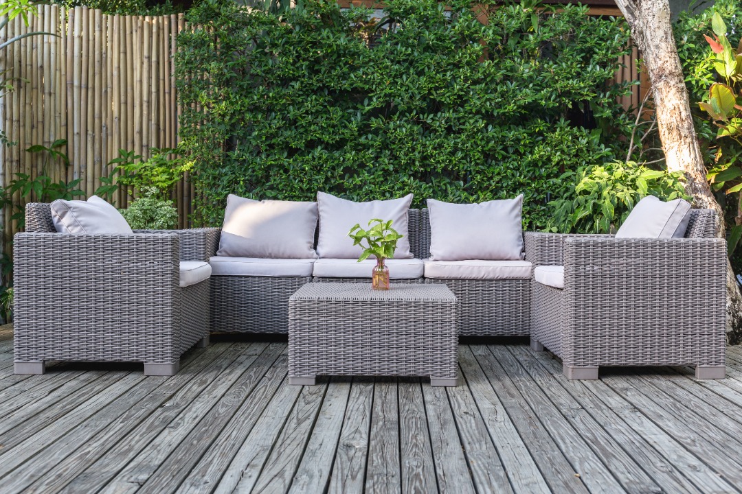 Cozy outdoor living space with wicker furniture, gray cushions, and lush greenery creating a relaxing backyard retreat.