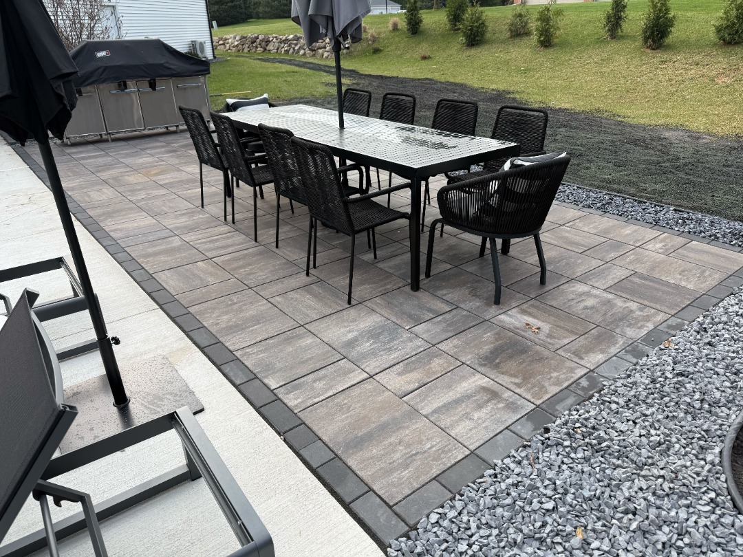 Spacious outdoor living space with modern paver patio, black dining set, and built-in grill for backyard entertaining.